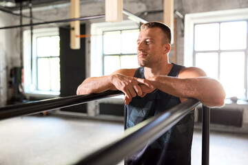 fitness, sport, training and lifestyle concept - young man exercising on parallel bars in gym