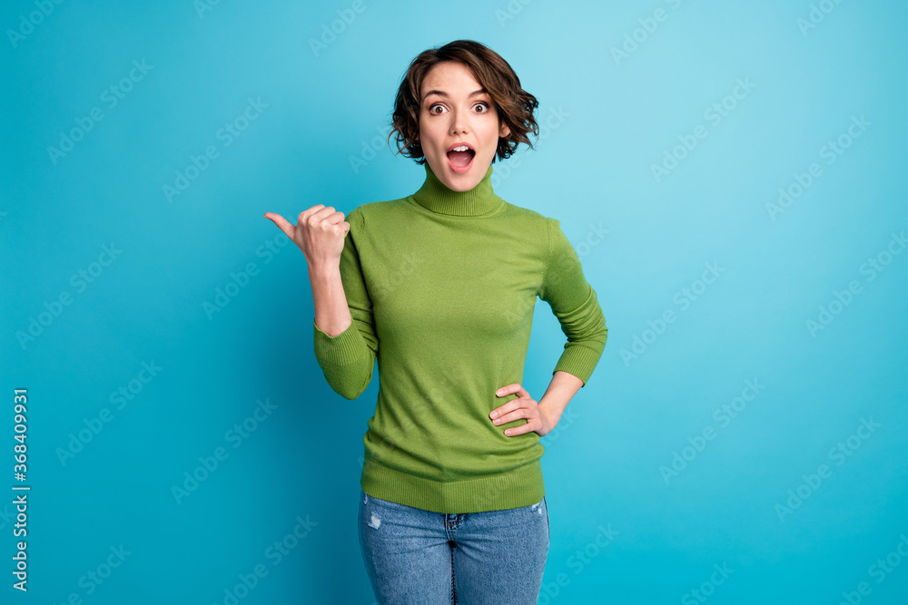 Portrait of astonished girl promoter point thumb finger copyspace impressed incredible ads direct way wear trendy sweater isolated over blue color background - obrazy, fototapety, plakaty 