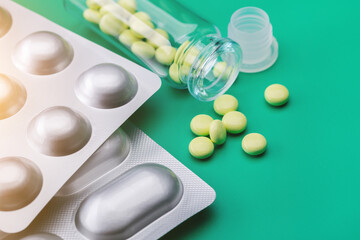 Yellow pills scattered from  bottle against  green background. The blister pack contains different tablets and capsules. Pharmaceutical industry. Pharmacy