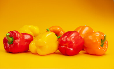 Colorful red, orange and yellow peppers paprika on yellow background