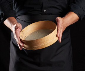 Wall Mural - man in black uniform holding empty vintage round wooden sieve for sifting flour