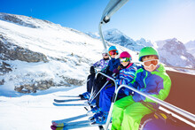 High Portrait Of Four Happy Kids In Vivid Ski Outfit Lifting On Chairlift On The Mountain Together And Smiling