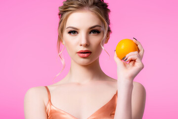 Wall Mural - elegant beautiful blonde woman holding ripe orange isolated on pink