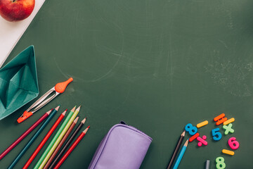 Wall Mural - top view of school stationery, paper boat and whole apple on green chalkboard