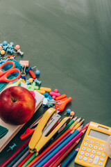 Wall Mural - High angle view of ripe apple on book near school stationery on green chalkboard