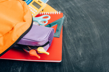 Wall Mural - Yellow backpack with multicolored school stationery on black chalkboard