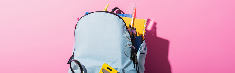 Wall Mural - horizontal image of blue backpack with school supplies and eyeglasses on pink