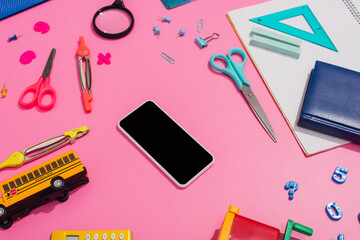 Wall Mural - high angle view of smartphone with blank screen near school bus model and stationery on pink