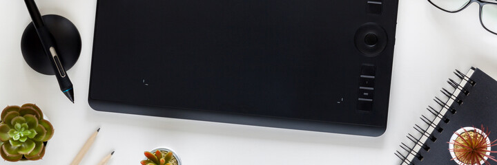 Fototapete - A graphics tablet in the center of a white desk. Office utensils all around. Notebook, succulents. Panorama.