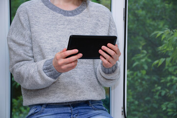 Caucasian woman with a black smartphone in her hands against  background of an open window.