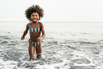 Wall Mural - Afro child having fun playing inside sea water during summer holidays - Childhood and travel vacation concept