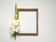 Flat lay composition with empty wooden frame and white gladioli flowers on white surface. From above, top view, copy space. 