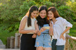 Three young Asian women as friends using phone together at the park