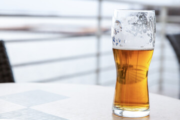 a transparent glass of golden beer drank with foam on the walls, rest in an outdoor cafe