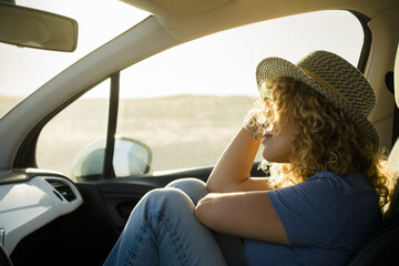 Wall Mural - one, beautiful curly woman enjoying her vacations outdoors traveling with a car - sunset and sunny day at the background - relaxed and serene person