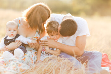 Family with children walking outdoors in summer field at sunset. Father, mother and two children sons having fun in summer field. People, family day and lifestyle concept