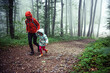 Mother and her young daughter trail hiking through misty forest.