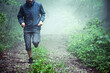 Close up of male athlete, wearing outdoor clothes, running through misty forest early in the morning. Copy space available.