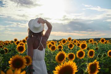 a young tanned girl in a white dress and hat walks in a field at sunset