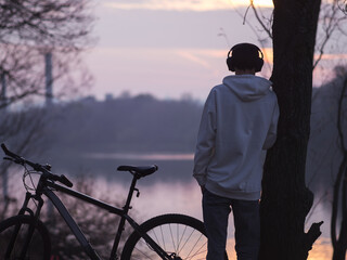 Wall Mural - A young man in a white hoodie listens to music and admires the purple autumn sunset. Ride a bike in the fall. Lonely man