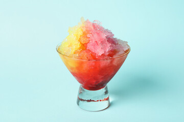 Rainbow shaving ice in glass dessert bowl on light blue background, closeup