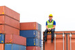 © godji10 - Portrait of confident inspector sitting on cargo container in shipping yard, Smiley engineer or happy dock worker wears hardhat and safety vest in port. Concept of transportation, logistics business.