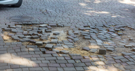 Wall Mural - The damaged asphalt road with potholes caused by freeze-thaw cycles during winter. Bad road. Broken paving slabs on the footpath