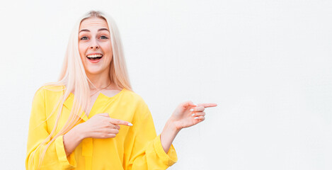 Advertisement concept. Positive, pretty woman with beaming smile in yellow shirt on white background is pointing with her two index finger and looking on empty copy space