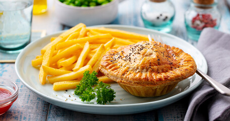 Meat pie with french fries on a plate. Wooden background. Close up.