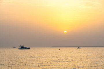 Stunning sunset over the Arabian Gulf, with luxurious yachts cruising near Jumeirah Beach in Dubai, UAE.