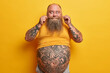 © wayhome.studio  - Horizontal shot of funny thick guy with big tummy, tattooes on arms and belly, twirls mustache, dressed in yellow t shirt, has obesity as drinks much beer and eats junk food. Fatso lazy male