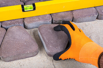 Laying paving stones on sand. Concrete cube in the hand of a builder.