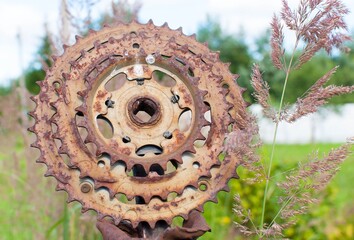 A small rusty metal wheel was put on an iron fence.