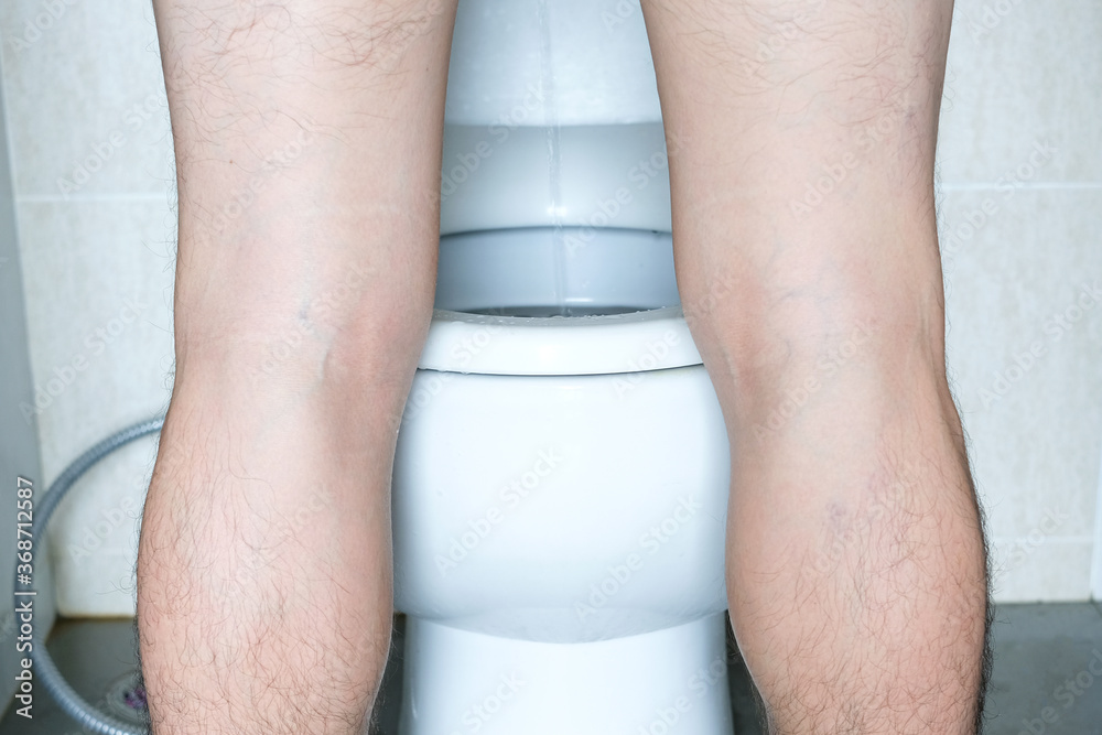 man-peeing-to-toilet-bowl-in-restroom-from-back-health-concept-stock