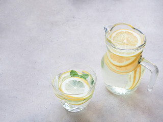 Lemons slice and water in glass, jar with mint leaves on grey background, drink for detox, and refresh the body..