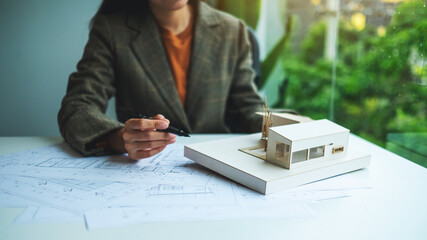 Wall Mural - A female architect holding and working on an architecture house model with shop drawing paper in the office