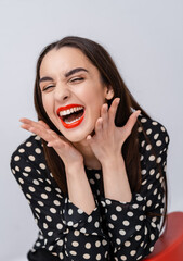 Canvas Print - Young beauty with perfect smile, red lips and white teeth. Girl holding finger near red lips. White background. Cheerful laugh.