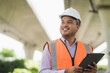 © Chanakon - Asian civil engineer operate with tablet to control working at construction. Worker wearing hard hat at highway concrete road site.