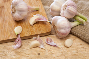 Fresh heads and cloves of garlic bulbs on cutting board and wooden table. Close up view