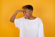© Roquillo - Young African American girl with afro short hair wearing white tshirt standing over isolated yellow wall very happy and smiling looking far away with hand over head. Searching concept.