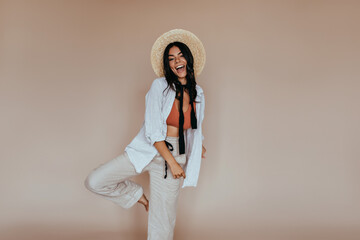 Wall Mural - Adorable woman in white costume dancing in studio. Indoor photo of amazing brunette girl in straw hat.