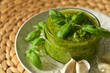 Italian green pesto sauce with leaf of basil on top in clear glass jar on a plate. 