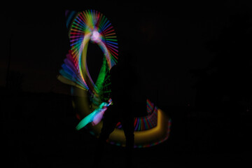 Long exposure shot, following the light trail from electrical juggling clubs that glow in changing colors, with the Juggler’s silhouette hidden between them.