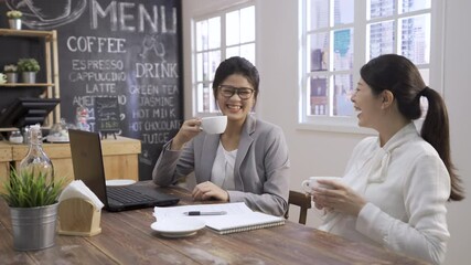 Wall Mural - cheerful two asian chinese women workers sitting at laptop computer in coworking. elegant lady colleagues discussing new project during collaboration in cafe meeting. partners drinking cup of coffee