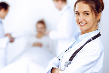 Wall Mural - Female doctor smiling on the background with patient in the bed and two doctors