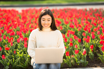 Asian woman using laptop, sitting on parapet