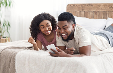 Happy black lovers celebrating success, holding smartphone