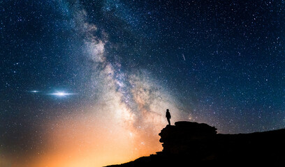 man standing in a high place looking up in wonder to the milky way galaxy. small silhouette of a man