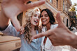 © Look! - Laughing blithesome woman with dark hair walking down the street with friend. Carefree blonde girl posing on city background.