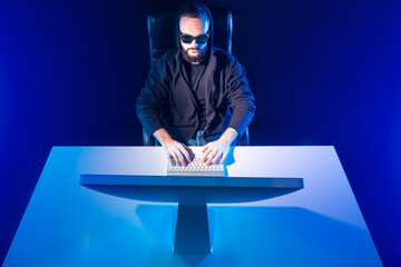 Poster - Blue background with a man at the computer. Symmetrical image of a person at a computer. A man in black clothes and glasses works on a PC.